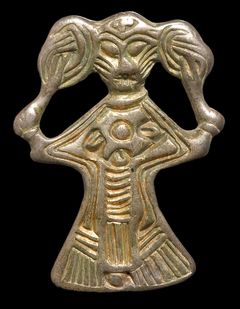 Kvindefigur af sølv, som kan være gudeninden Freja. Kvinden river sig i håret, der er bundet op i to knuder. Motivet har rod i 500-tallets billeder af byzantinske kejserinder, men fik sit eget udtryk på nordiske smykker fra den sene jernalder og vikingetid. Hårrivningen kan være et billede på tab og sorg, men måske også på vrede.