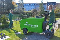 På Brønshøj Kirkegård kører Sofie Kruse og Freja Busch fra OKNygaards driftsafdeling i Glostrup rundt på en af virksomhedens el-ladvogne. El-ladvognene bliver især brugt på kirkegårde og hospitaler, hvor der er begrænset plads og behov for ro.