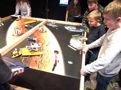 Elever fra 5. Klasse har under Lego Space Challenge i marts 2022 programmeret EV3 robotten til at løse missioner på Spacebanen. De dyster to hold af gangen og det hele livestreames på storskærm lige bagved. Store elever fra Kobberbakkeskolen afd. Sjølund holder øje med om reglerne følges og giver point.