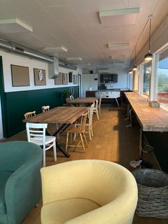Huset er opvarmet og indrettet med højborde langs vinduerne ud mod Travbyen og borde-bænke sæt ude og inde. Atmosfæren er hyggelig og uformel. Foto: Billund Kommune