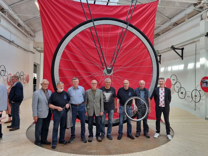 Det store cykelhjul i femdobbeltstørrelse, de frivillige, der har bygget det og værkstedskoordinator i Historie Haderslev, Frede Poulsen yderst til højre. Frede har desuden stået for opbygningen af resten af udstillingen.