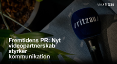 Mikrofon med logoet "ritzau" placeret på en sofa, ved siden af en plante. Teksten siger: "Fremtidens PR: Nyt videopartnerskab styrker kommunikation".