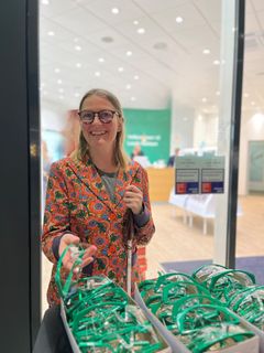 En kvinde i farverig jakke står ved siden af en skål med sikkerhedsbriller og smiler til kameraet.