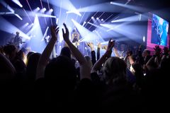 Koncertscene med optrædende kunstner og en entusiastisk publikumshav med hænderne i vejret.