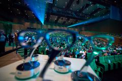 En scene med et publikum sidder i en stor sal, med brilleformede priser i forgrunden.