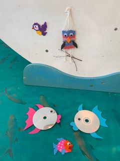 Forskellige håndlavede dekorationer af perler, garn og cd'er forestillende fugle og fisk.