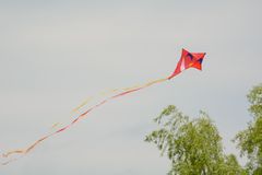 Rød drage med lange haler flyver højt på en klar himmel over trætoppe.