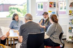 En gruppe ældre mennesker sidder rundt om et bord og diskuterer i en læseklub.