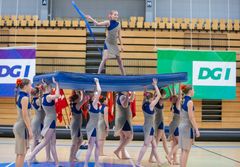 En gymnastiktrup i kostumer udfører en formation i en sportshal.