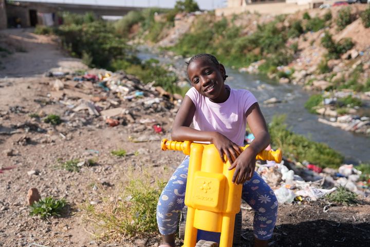 10-årige Ompfuna Nkhumeleni sidder på sin plastikmotorcykel ved den forurenede Juskei-flod i Silvertown, en af de fattigste og mest trængte townships — i skarp kontrast til det nærliggende, velhavende Sandton.