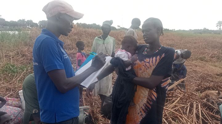 En Plan-medarbejder tager imod en kvinde og barn, der er flygtet over grænsen via en flod. Flygtninge kommer både ind i Etiopien og Uganda. Foto: Plan International