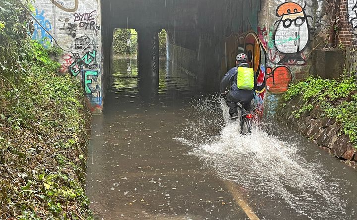 Foto af cyklist, der cykler i en masse vand efter et skybrud.