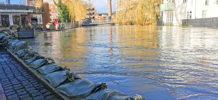 Foto af en å med sandsække, der skal forhindre oversvømmelse i nærliggende bygninger.