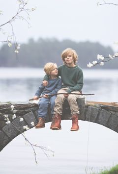 To unge drenge sidder tæt sammen på en bro med blomstergrene i forgrunden.