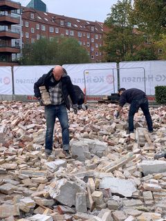 To mænd samler brugte mursten på en byggeplads.