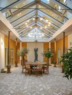 Et rum i Frichsparken med glasloft, træer i potter og et sildebensmønster på gulvet.