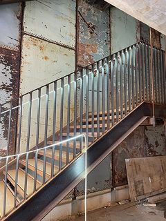 En trappe med metalgelænder foran en rustik, patineret væg i industriel stil.