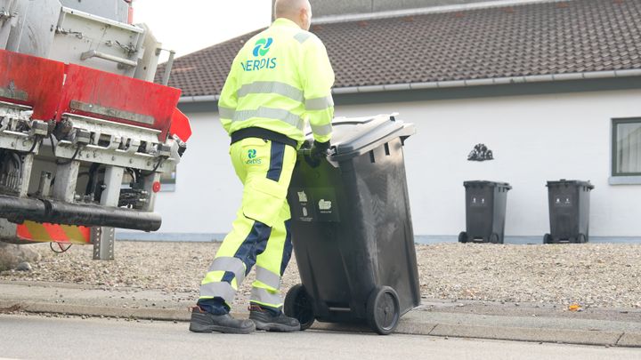 Skraldemand kommer gående med en affaldsbeholder. På adgangsvejen er løse sten.