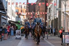 Ryttere i blå uniformer rider gennem en by med danske flag hængende i gaderne.