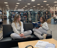 To piger der læser bøger, siddende i en sofa på biblioteket