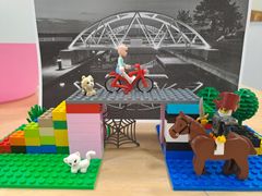 Lego scene med en person på cykel på en bro og en figur på hest nedenunder.
