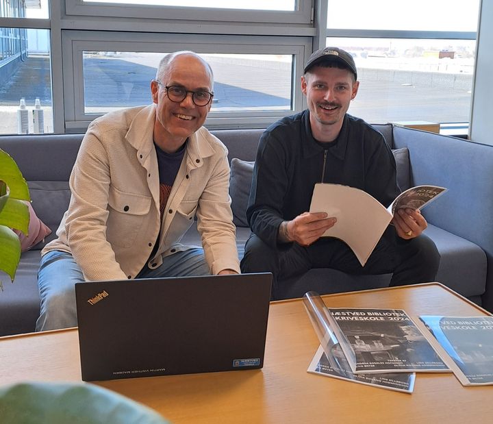 To personer sidder ved et bord med en bærbar computer og papirer.
