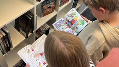 To børn læser tegneserier foran en bogreol på et bibliotek