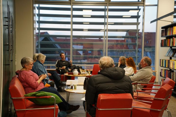 En gruppe mennesker sidder ved små borde og taler sammen