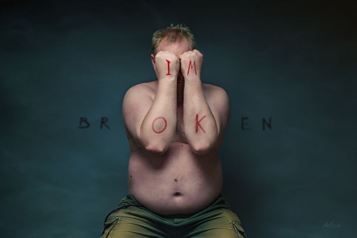 En person sidder med bar overkrop og gemmer ansigtet med hænderne. Ordene "IM BROKEN" er skrevet hen over billedet.