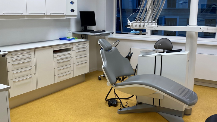 Tandlægekontor med en tandlægestol, skuffer og et skrivebord med en computer.