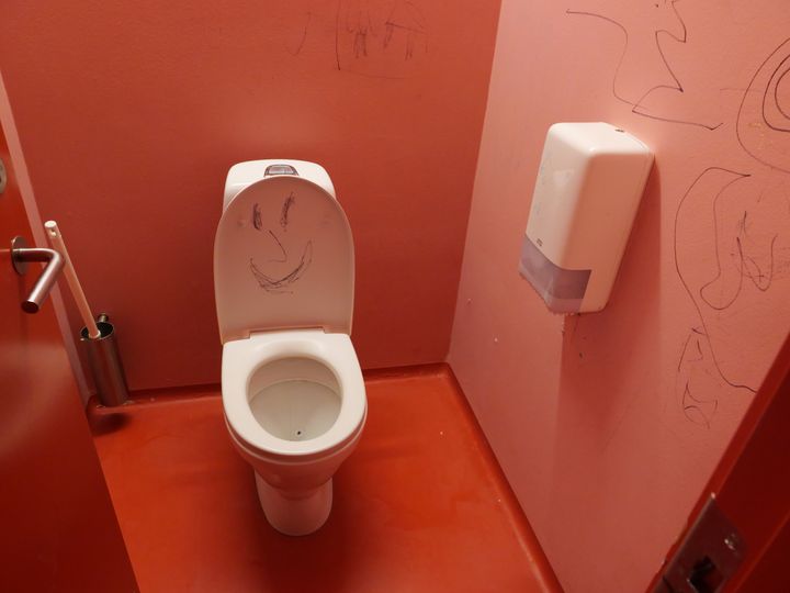 Toilet i et lille rum med lyserøde vægge. Toilettet har en tegning af et smilende ansigt på sædet.