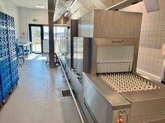 Opvaskemaskine i et storkøkken med blå kasser stablet til venstre.