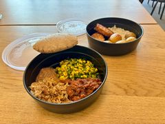 To skåle med forskellige retter, herunder brød, grøntsager og kød, står på et træbord.