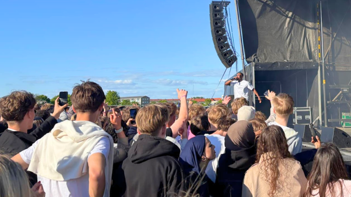 En gruppe mennesker står foran en udendørs scene ved en festival.