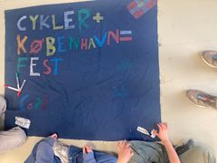 Børn maler et blåt banner med teksten "Cykler + København = Fest".