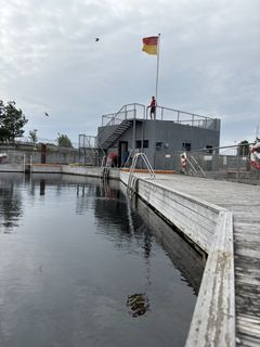 Billede af Havnebadet Sluseholmen med en badebro, livreddertårn og flag. Maj 2025