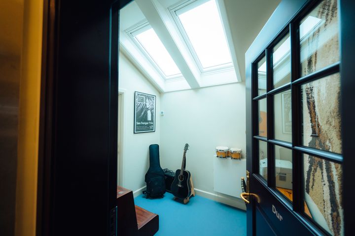 Musiklokale med guitar, trommer og plakat på væggen.