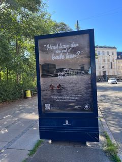 Reklameplakat for nye havnebaderåd, der viser to personer i vandet med bybygninger i baggrunden.
