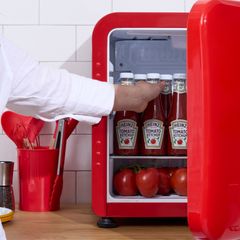 Person placerer Heinz tomatketchupflasker i et lille rødt køleskab.
