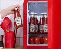 Alt-tekst: En hånd placerer en flaske Heinz tomatketchup i et køleskab fyldt med flere andre flasker tomatketchup.