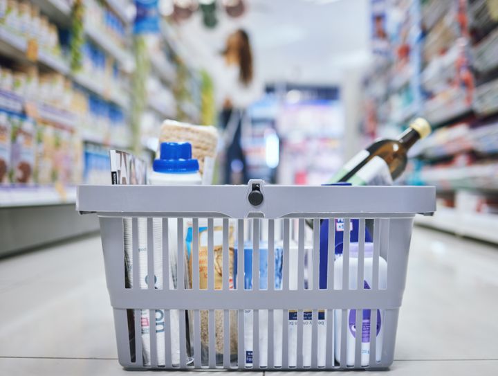 En indkøbskurv fyldt med dagligvarer i en supermarkedsgang.