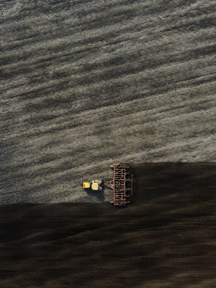 En mark set fra oven med en gul traktor, der pløjer jorden.