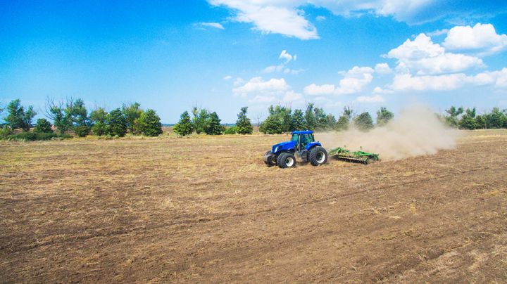 Traktor pløjer en støvet mark under en blå himmel.