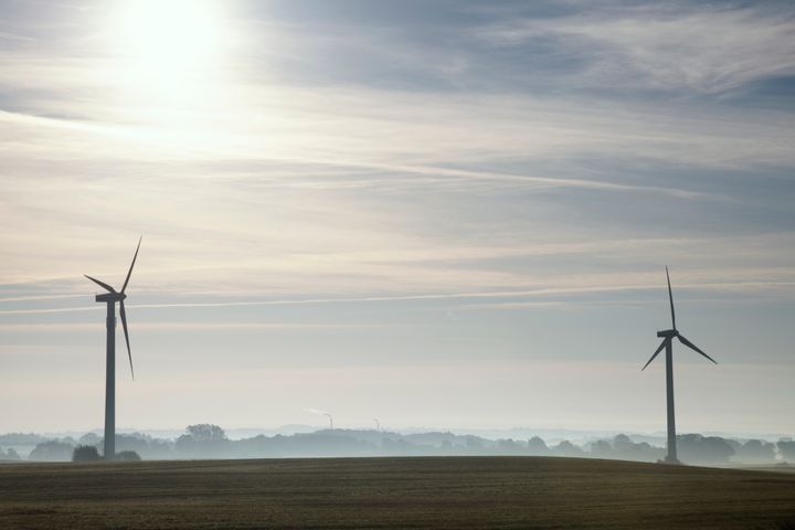 To vindmøller i et åbent landskab under en delvist overskyet himmel.