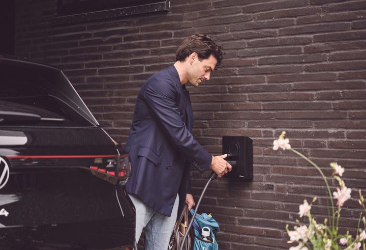 En mand sætter sin elbil til opladning ved en ladeboks på husets mur.