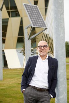 Jakob Bundgaard, direktør i NRGi Renewables, står udendørs foran NRGis kontor ved en stolpe med solpanel.