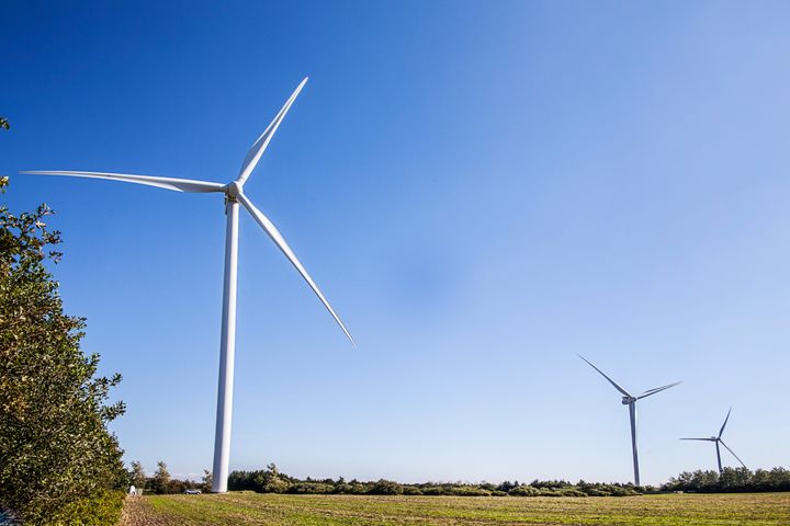 Tre vindmøller står på en grøn mark under en klar blå himmel.
