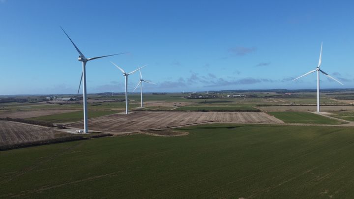 Vindmøller i et landskab med marker og blå himmel.