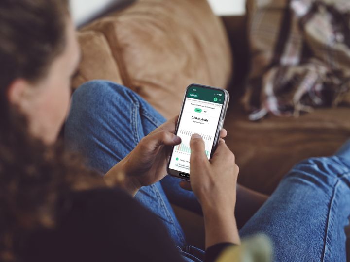 En kvinde tjekker elprisen i NRGi's app på sin mobiltelefon. Skærmen viser den aktuelle timepris og en graf over dagens prisudvikling.