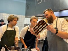 Værkstedsmester på Chokoaldeværkstedets viser to elever, hvordan man støber chokolade i en form som en del af chokoladens vej fra bønne til bar.